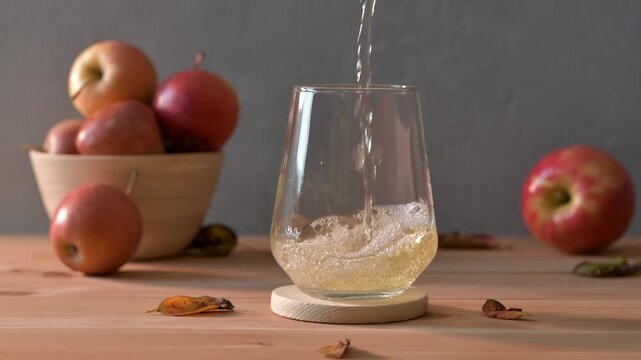 Sparkling apple cider pours into clear glass with bowl of fresh apples on wooden table, cozy autumn refreshment for seasonal menus.