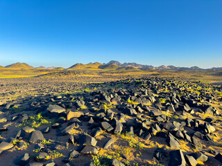 Stone desert in Saudi Arabia, black stones in the foreground with mountains in the background.