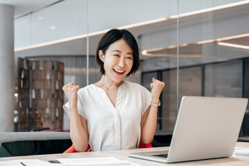 Happy Asian young businesswoman winner showing triumph yes gesture. Emotional business woman...