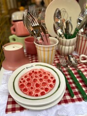 Table setting with assorted cutlery, pink and striped cups, plates, and checkered cloth