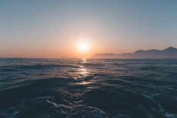 Sunrise over a tranquil ocean, hazy mountains in the distance