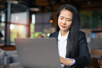 Young Asian professional businesswoman using laptop to manage marketing and using computer to manage digital data and sitting in modern office.