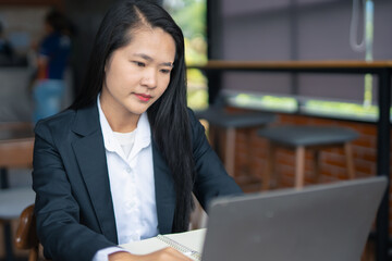 Young Asian professional businesswoman using laptop to manage marketing and using computer to manage digital data and sitting in modern office.