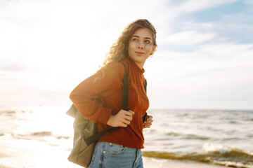 A cute woman with a briefcase is standing on the seashore or ocean and enjoying the sunset....