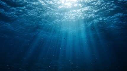 Fototapeta premium Sunlight streams through ocean waves, creating a mesmerizing play of light and shadow in deep blue waters.