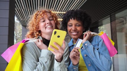Two joyful young women happily enjoying their shopping experience as they excitedly use a smartphone to share their latest finds and moments of joy, showcasing their friendship and delight. - Powered by Adobe