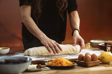 A person in a black shirt kneads dough on a floured table. Bowls of ingredients, eggs, and a lemon...