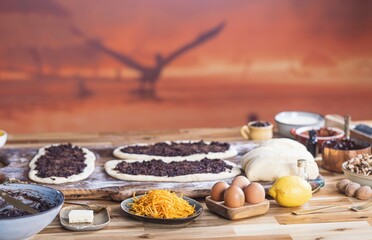 A wooden table holds dough, eggs, lemon, butter, jam, and other ingredients used to bake sweet...