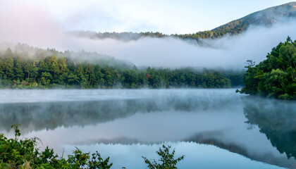 Fototapeta premium Serene Lake Surrounded by Lush Forests and Rolling Hills in Morning Mist