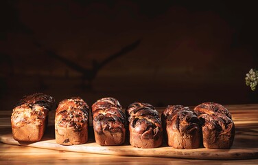 Seven beautifully baked babka loaves sit closely together on a light wooden board, ready to be...