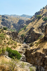 A narrow mountain river meandering between steep cliffs in Boshkyzylsay, Uzbekistan, with rocky banks and summer sunlight, July 2025