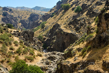 A narrow mountain river meandering between steep cliffs in Boshkyzylsay, Uzbekistan, with rocky banks and summer sunlight, July 2025