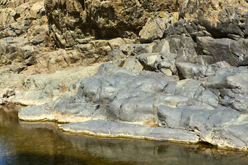Rock face with moss and lichens by the water’s edge of a mountain stream in Boshkizilsay, Uzbekistan. Sunny summer day, view of the natural shore and water reflection