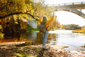 A rear view of a young female hiker with a backpack on a hiking trail in autumn enjoying sunlight....