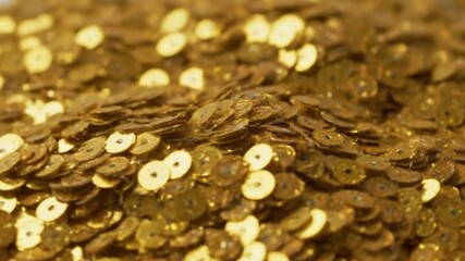A closeup shows a dense pile of small circular golden sequins with central holes creating a textured shimmering surface - Powered by Adobe