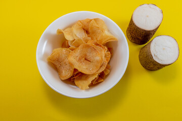 Cassava Crisps on Plate with Fresh Cassava Root over Yellow Background