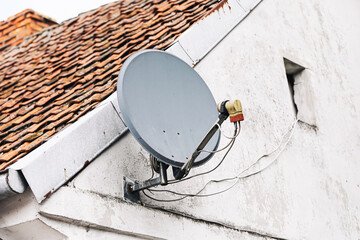Satellite dish on old building wall. Gray antenna mounted on exterior facade under sloped roof with...