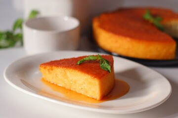 A slice of caramel bread pudding served on a white plate, topped with fresh mint and drizzled with golden caramel sauce