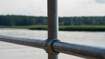 Close-up of a metallic railing near a river surrounded by greenery on a sunny day