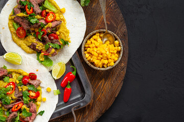 Mexican tacos, tortilla with beef, vegetable sauce, corn and tomatoes on the black background top view