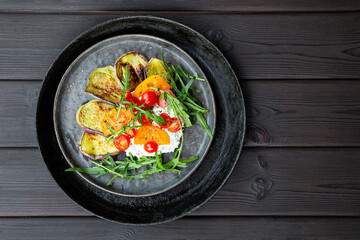 Salad with fried eggplant, cream cheese, tomatoes and arugula on black background. Vegetarian food