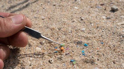 Investigating coastal pollution: Macro shot of tweezers carefully picking up a single, tiny microplastic fragment from the sand, symbolizing scientific research into environmental contamination.