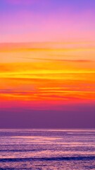 Fototapeta premium A vibrant sunset paints the sky in shades of orange, pink, and purple, reflecting on the calm ocean waves, while fluffy clouds add texture to the scene.