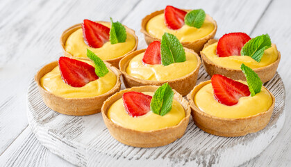 Mini mango cream tarts with strawberry and mint on white wooden board
