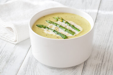 Creamy asparagus soup in white bowl with swirl and toasted ciabatta