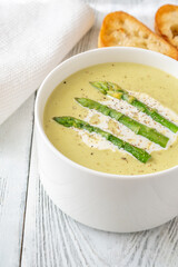 Creamy asparagus soup in white bowl with swirl and toasted ciabatta