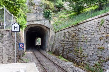 Railway tunnel entrance with tracks disappearing into the darkness, seen from the Schloss Laufen am Rheinfall train station platform