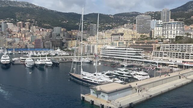 Elevated view of Port Hercule in Monte Carlo, Monaco, featuring luxury yachts, waterfront buildings, and the famous harbor surrounded by the hills of the French Riviera. The marina is one of the Medit
