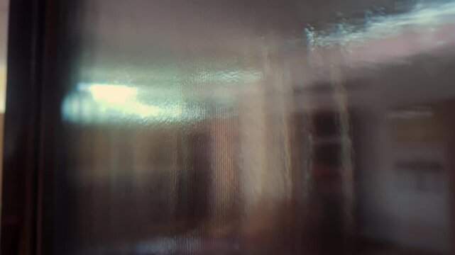 Blurry view through frosted textured glass surface showing distorted shapes of interior room, evoking abstract mystery, depth, and softened architectural forms