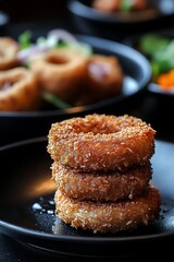 Stack of golden brown crispy fried onion rings on a dark plate appetizer breaded