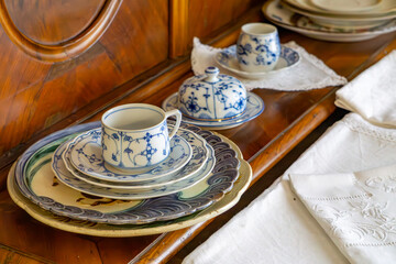 Antique porcelain cup and plate set with a blue pattern, arranged on a wooden sideboard with a lace...