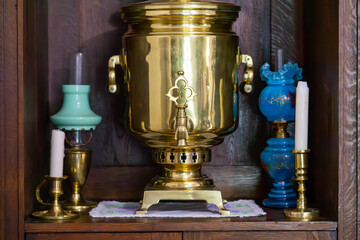 Antique items – a golden samovar on a wooden shelf, accompanied by candlesticks and decorative oil lamps.