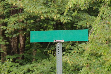 closeup of a blank green road sign on a metal post isolated against a green woodland forest background. transportation, business or creative element with copy space
