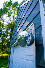Large Disco Ball Lit Up by the Sun and Casting Shimmering Light Reflections Onto Blue House With...
