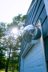 Large Disco Ball Lit Up by the Sun and Casting Shimmering Light Reflections Onto Blue House With...