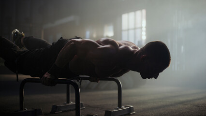 Determined male athlete performing intense calisthenics workout on parallel bars in gym