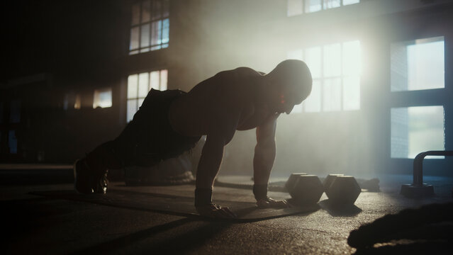 Muscular athlete doing push-ups in a dramatic gym setting with backlight