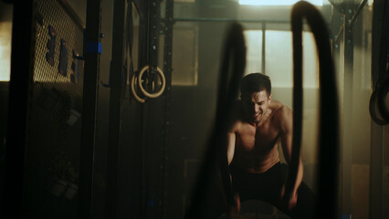 Determined athlete lifting heavy weights in dark gym