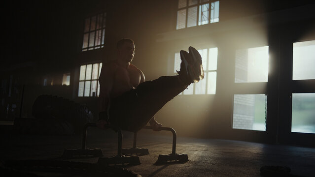 Determined male athlete performing l-sit exercise on parallel bars in gym