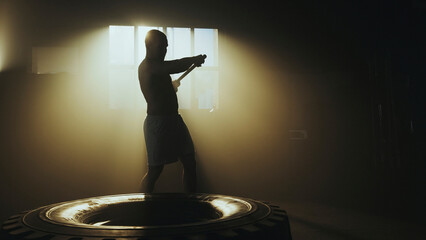 Athlete using hammer on tire during cross training workout in dramatic lighting