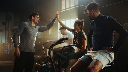 Athletes giving high five after exhausting air bike exercise in gym