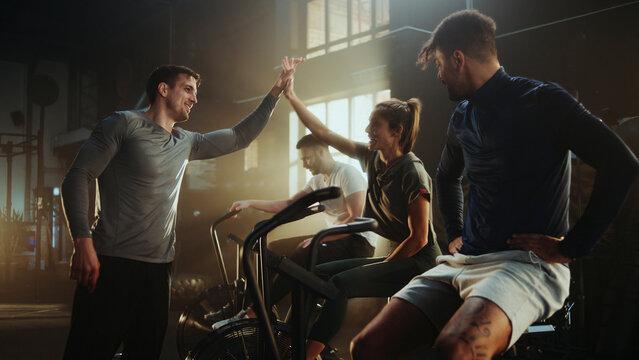 Athletes giving high five after exhausting air bike exercise in gym - Powered by Adobe