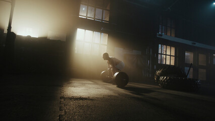 Determined male athlete lifting heavy barbell in dramatic gym setting