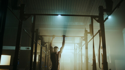Determined male athlete performing pull-ups in dramatic gym setting