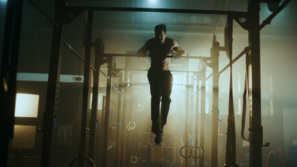 Determined male athlete performing pull-ups in dramatic gym setting