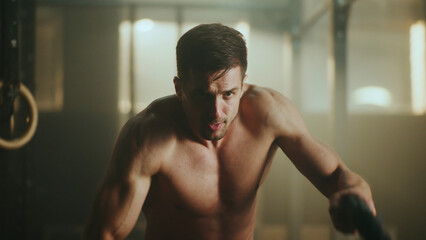 Determined male athlete doing battle ropes exercise in crossfit gym